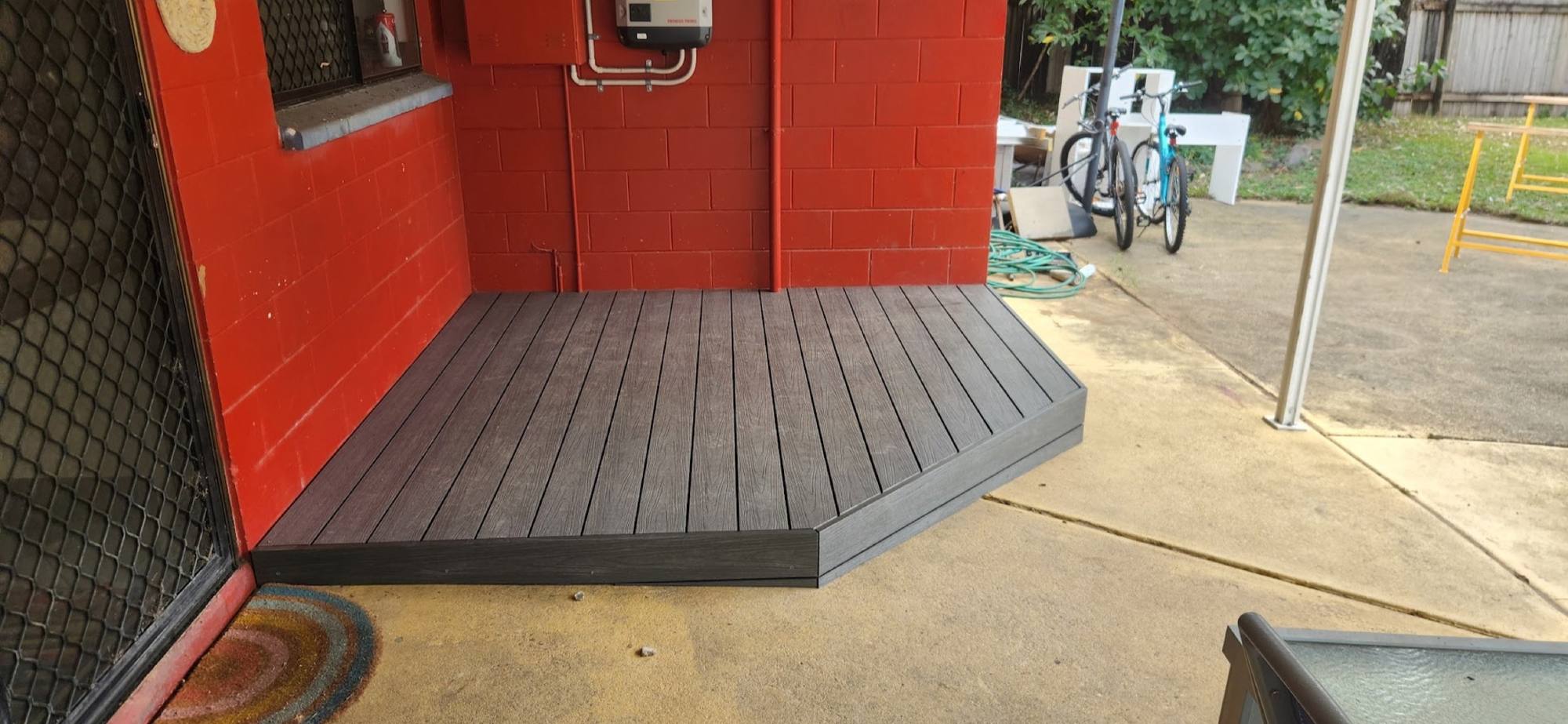 A composite deck landing built against a red painted block wall beside a driveway