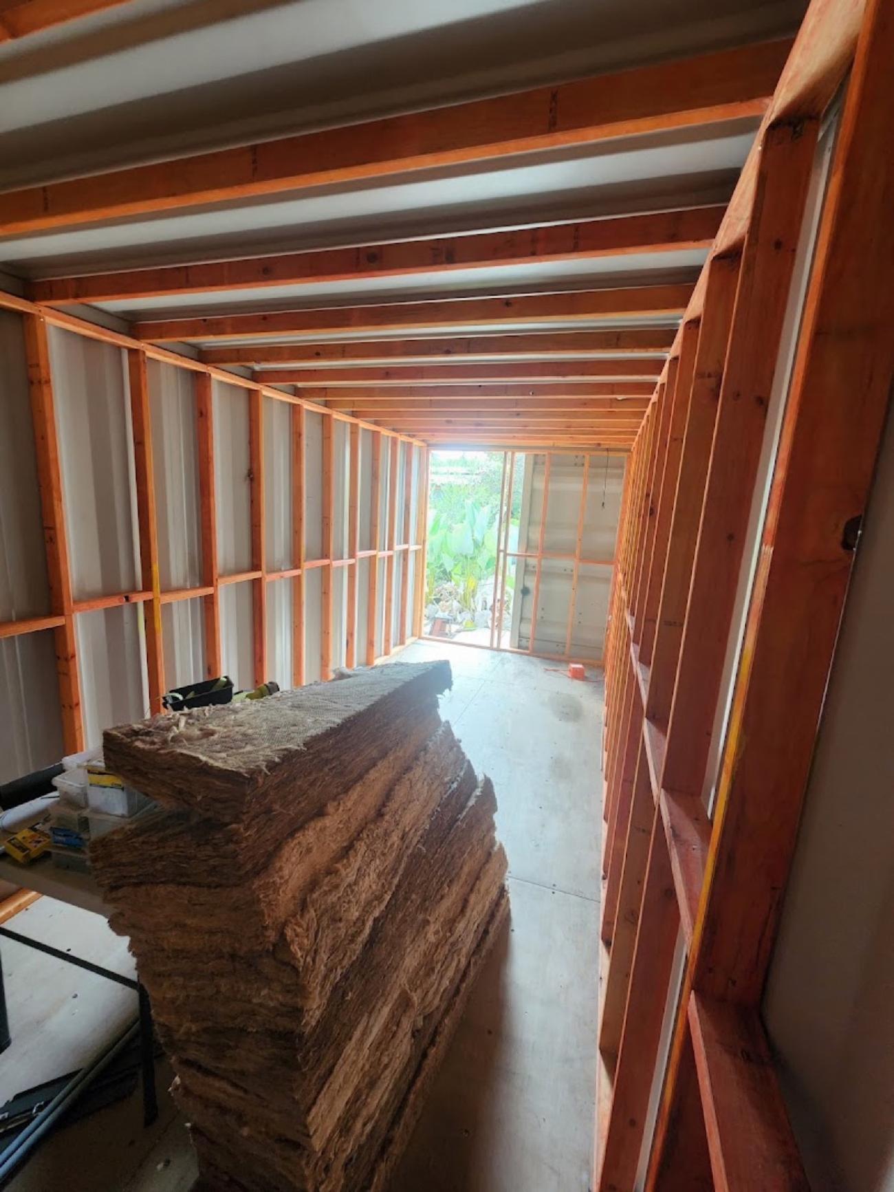 The inside of a shipping container fitted out with timber wall framing and stacked insulation batts