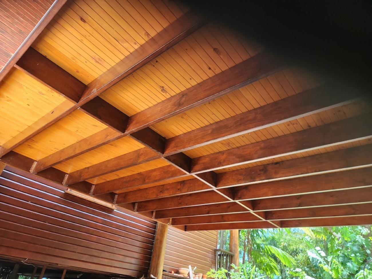 The underside of a timber pergola roof with stained rafters and a lined ceiling