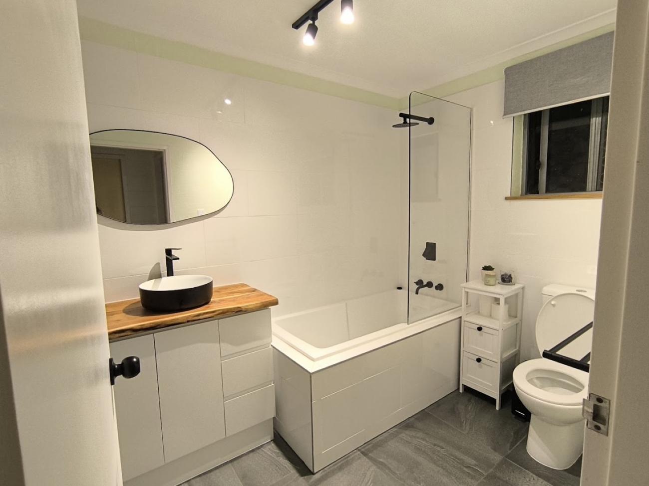 A renovated bathroom with a white vanity, timber benchtop and a glass shower screen