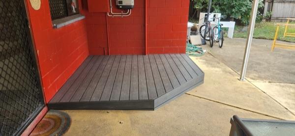 A composite deck landing built against a red painted block wall beside a driveway