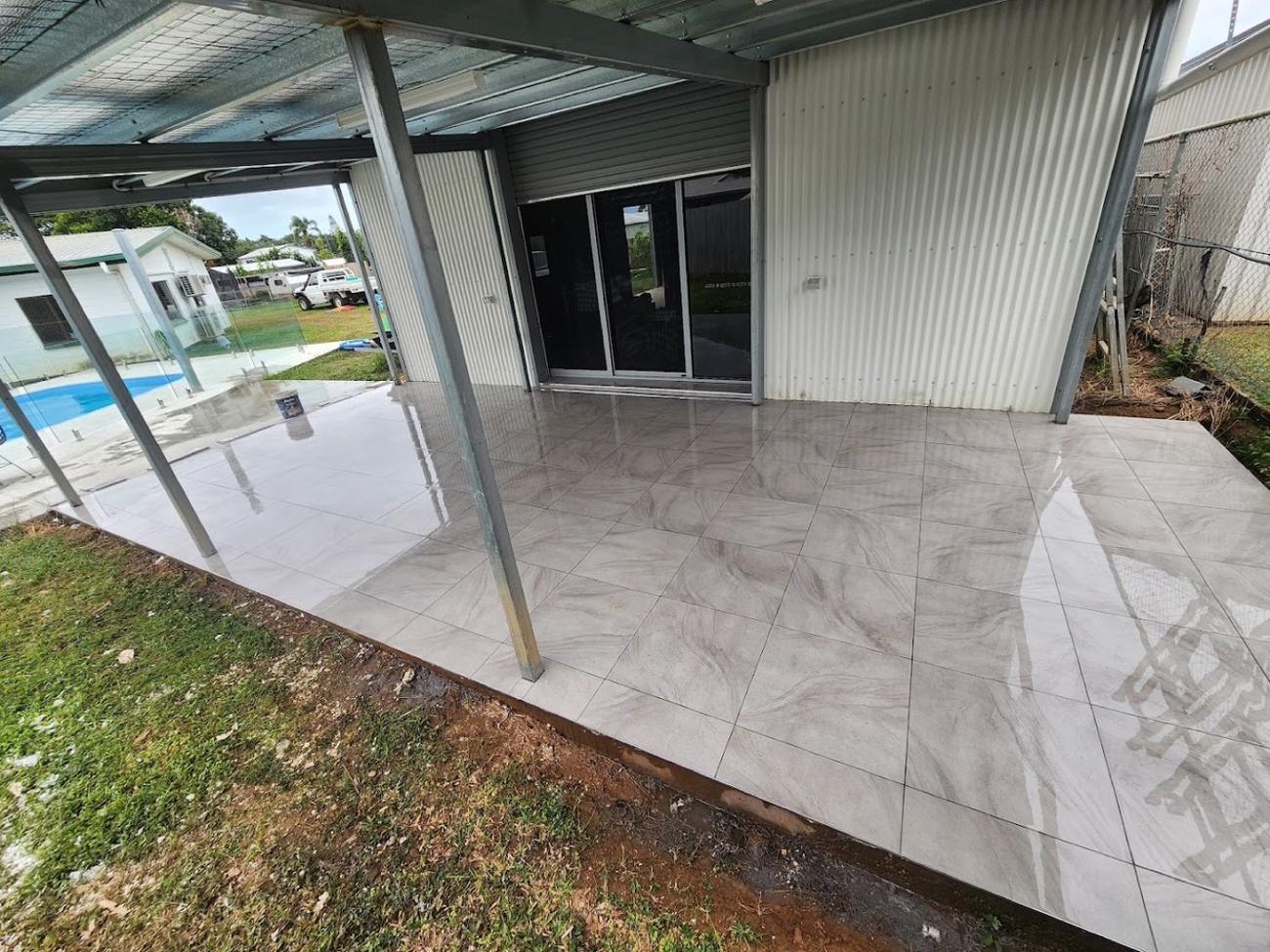 A large tiled outdoor area under a steel patio frame beside a pool